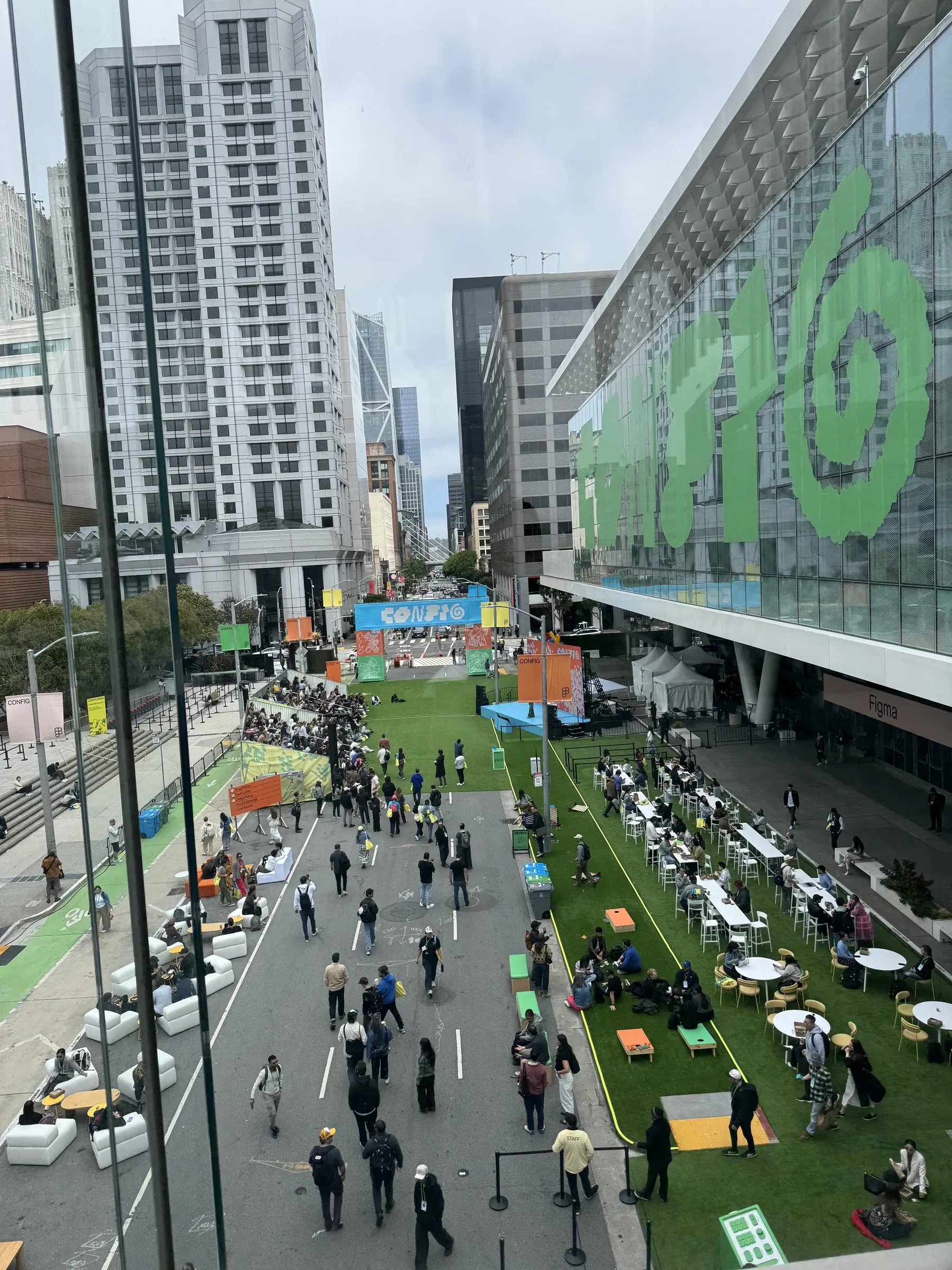 Overhead view of the closed-off street outside Moscone Center, with a giant green Config logo on the glass facade and crowds on the astroturf below